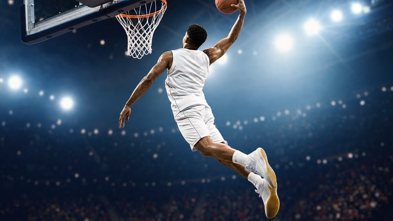 A basketball on a hardwood court beneath the hoop under arena lighting